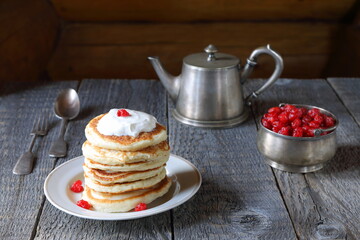 Stack of pancakes with sour cream is in front of silver utensils on the wooden background. 