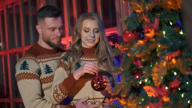 Handsome man and beautiful woman decorate New year tree with christmas balls. Spanding holidays together.