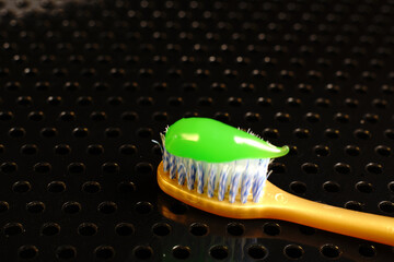 A yellow toothbrush with light bristles lies on a black metal table. And bright green toothpaste....