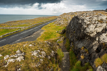 Fototapeta na wymiar Small narrow asphalt road by the Atlantic ocean. Burren area, West coast of Ireland. Warm sunny day. Cloudy sky