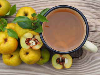 Ripe yellow fruit of the shrub Chaenomeles japonica and a drink in a mug on a wooden background top...