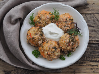 Meatballs with meat and rice, sour cream sauce, spicy fresh herbs in a plate with a napkin on a wooden table, top view. Recipe for a light, hearty and delicious meal for lunch, closeup