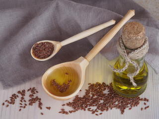 Flaxseed oil, linseeds in a wooden spoon and oil in a bottle with a linen napkin on a wooden background, top view. Natural healthy oleum lini with omega and vitamins for vegetarian diets