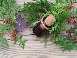 Thuja branches, herbal oil and flavored candles on a wooden background, top view. Natural medicinal plants for use in therapy, alternative medicine, homeopathy and cosmetology