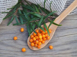 Fresh berries and sea buckthorn leaves in a wooden spoon on a wooden table with a napkin, top view. Healthy orange fruits hippophae rhamnoides plants with lots of vitamin C