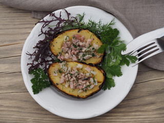 Fried potatoes in the skin with bacon, herbs in a white plate with a fork and knife on a wooden table, top view. Delicious healthy dish with vegetables, cooked on the grill