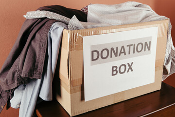 cardboard box with donation clothes and different objects on wood, donation concept
