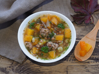Pumpkin soup with meatballs and lentils in a white bowl, napkins autumn leaves on a wooden background, top view. Recipe for seasonal healthy soup for proper nutrition