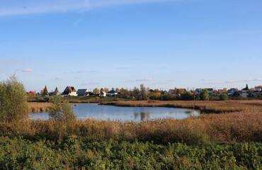 Fototapeta na wymiar lake with a reservoir near the houses in the village in autumn rural landscape in nature