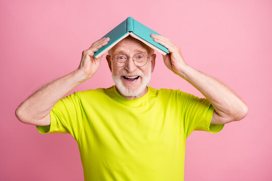 Portrait of cute optimistic pensioner hold copybook on head wear spectacles green color t-shirt isolated on pastel pink color background