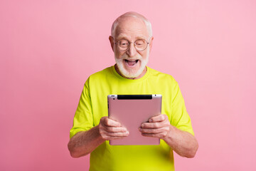 Portrait of optimistic pensioner hold tablet wear spectacles green color t-shirt isolated on pastel pink color background