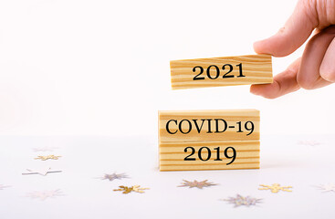 Hand holding wooden cube with text 2021 ,Covid-19, 2019 on table background. New Year concepts with...
