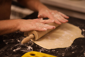cook rolls out the dough, men's hands work with the dough, cooking dough for dumplings, cook's...