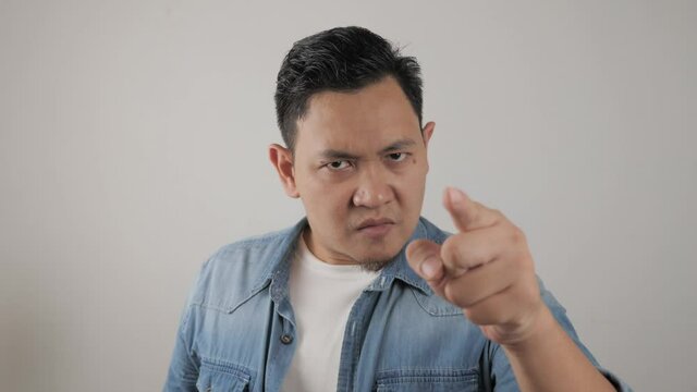 Portrait of Asian man showing cynical unhappy angry facial expression pointing forward, giving warn