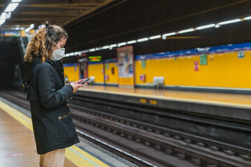 New normal. Young girl using her smartphone in the subway. Teenager using her smartphone in the subway. Teenager with a mask. Young girl with protective mask. Pandemic.