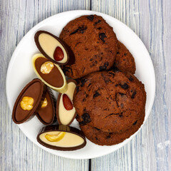 Chocolate chip cookies and chocolates on a white plate. Light wooden table in Provence style. Square format