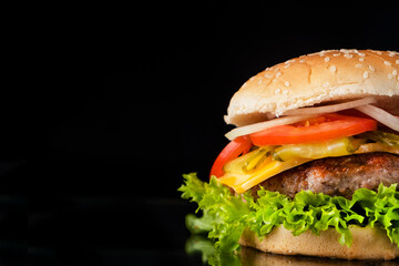 Tasty beef burger with cheese, onion, tomato and lettuce isolated on black. Copy space