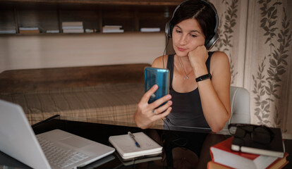 Shot of pretty young woman using her mobile phone while working with laptop sitting at home.
