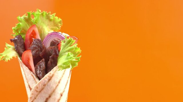 Shawarma or doner kebab moves on an orange background. Shawarma is made with tortilla, beef, tomato, onion and lettuce.