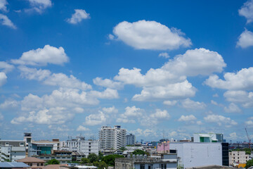 Fototapeta na wymiar White fluffy clouds on vivid blue sky above a city, view from rooftop 