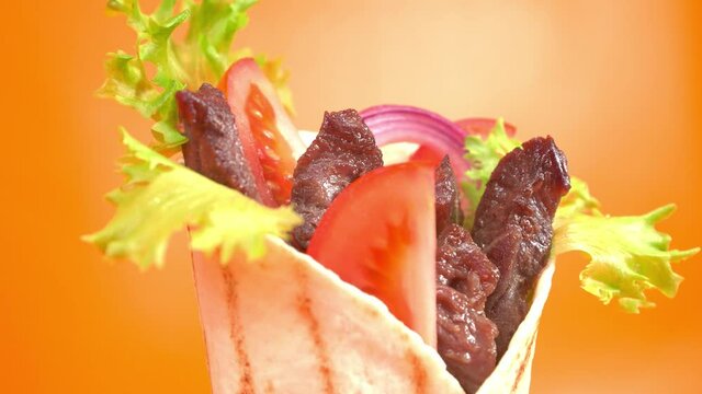 Shawarma or doner kebab moves on an orange background. Shawarma is made with tortilla, beef, tomato, onion and lettuce.