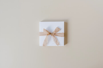 Paper gift box with bow tie on pastel beige background. Top view, flat lay. Christmas / New Year holiday surprise.