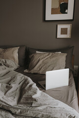 Modern interior design concept. Hygge styled bedroom with grey washed linen bedclothes, pillows, laptop. Minimalistic nordic living room.