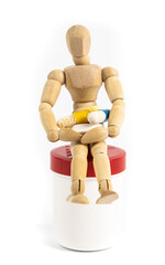 Small wooden figure sits on a pill box and holds various tablets in his arms, white background and copy space