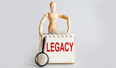 Wooden man shows with a hand to white notepad with text LEGACY