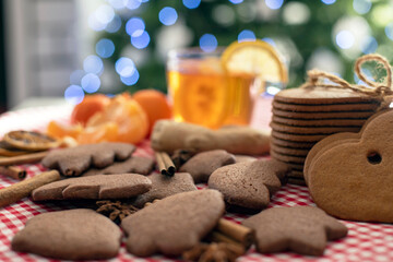 christmas gingerbread cookies and cinnamon on a red checkered tablecloth next to citrus tea and ginger on the background of a christmas tree