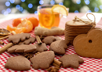 Fototapeta na wymiar christmas gingerbread cookies and cinnamon on a red checkered tablecloth next to citrus tea and ginger on the background of a christmas tree