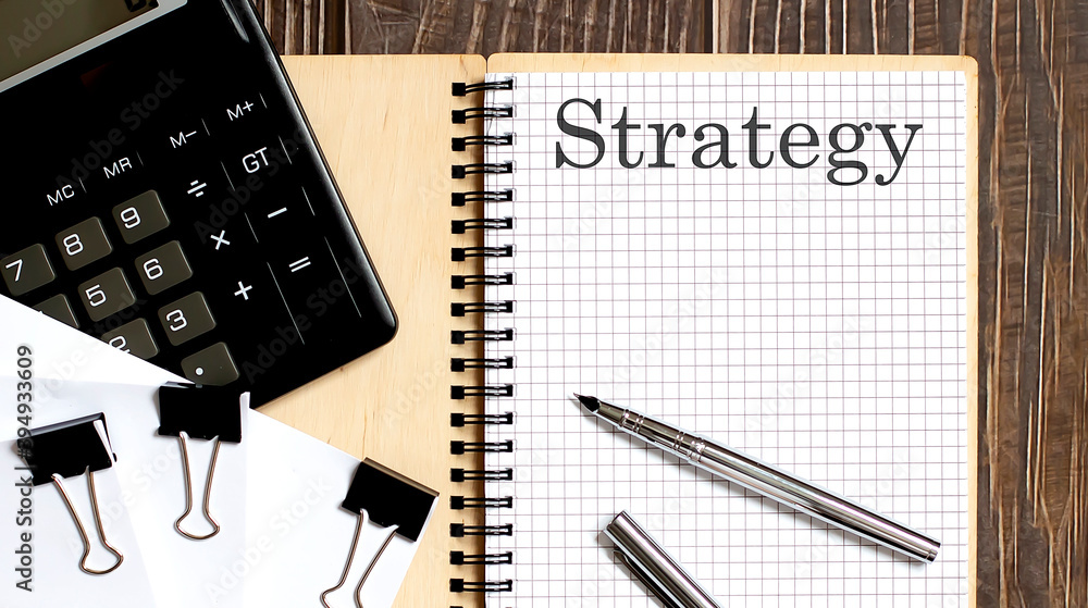 Poster notepad with text strategy on the wooden background with clips, pen and calculator