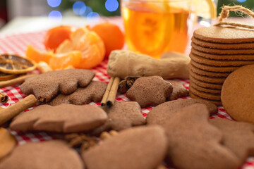christmas gingerbread cookies and cinnamon on a red checkered tablecloth next to citrus tea and ginger on the background of a christmas tree