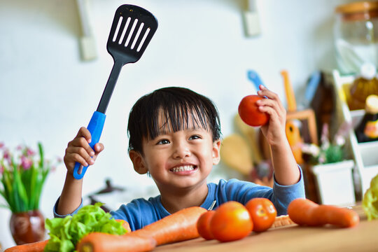 Boy Holding Tomato And Utensil In Kitchen At Home
