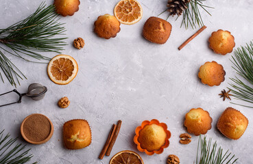 Fototapeta na wymiar A frame of delicious and fragrant vanilla cupcakes on a light background. Sprigs of pine, cinnamon sticks, orange, nuts, culinary accessories. A place for text.