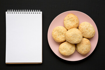 Homemade Flaky Buttermilk Biscuits on a pink plate, blank notepad on a black surface, top view. Flat lay, overhead, from above. Copy space.