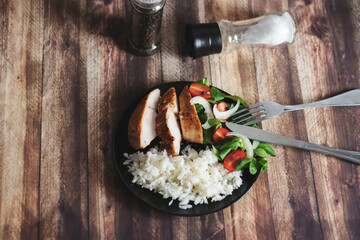 Ready chicken breast with rice and salad. All food on a black plate