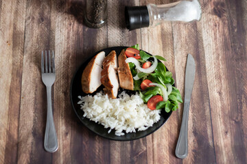 Ready chicken breast with rice and salad. All food on a black plate
