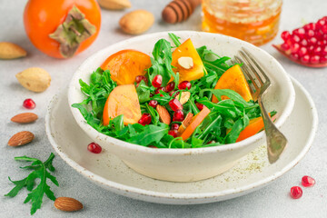 Delicious salad of fresh arugula, persimmon, pomegranate and almonds with a dressing of olive oil and honey. Healthy diet food. Selective focus