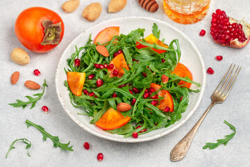Delicious salad of fresh arugula, persimmon, pomegranate and almonds with a dressing of olive oil and honey. Healthy diet food. Selective focus