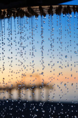 Plakat Water pouring from the outdoor beach shower head on blurred sunset seascape background, selective focus