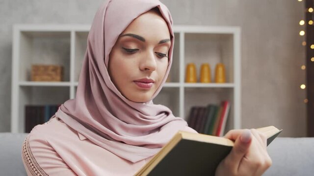 Close-up portrait of young and attractive muslim girl in hijab. Middle Eastern woman is sitting in front of the camera and reading the book.