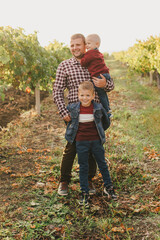 Happy father and his little sons taking a walk in vineyard at sunset.