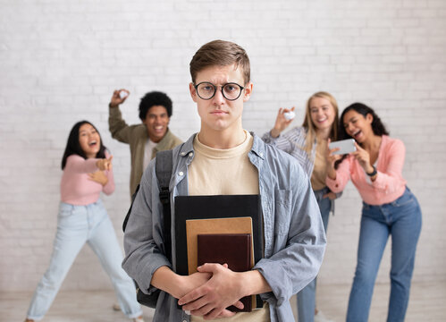 Humiliation and bullying at school. Focus on sad young guy in glasses and notebooks