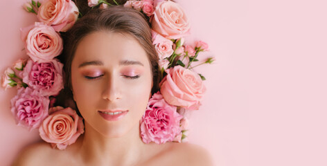 Close up portrait of beautiful woman face wih bright make up and perfect skin posing with roses on pink background.