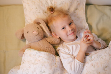 Cute child little girl posing in bed with white linen hugging her soft toy.
