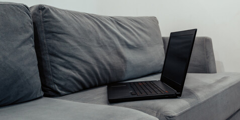 black laptop on a gray sofa white walls remote work freelance