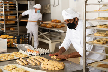 man in chefs uniform kneading dough in bakery during quarantine