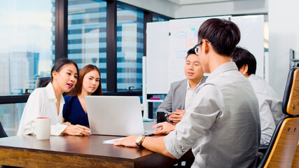 Group of Asian business people work together in team brainstorm discussion using laptop computer in office. Corporate business, coworker teamwork, or financial consultant meeting concept