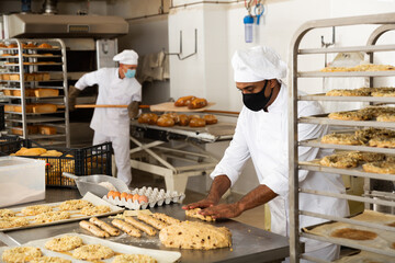 Portrait of male baker in face mask working with dough and forming baguettes